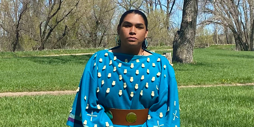 Brown skinned person wearing a blue embroidered dress.