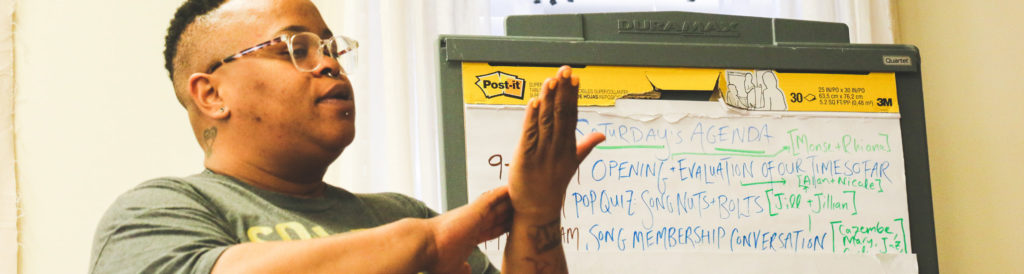 Someone teaching, there is a white board in the background with writing on.